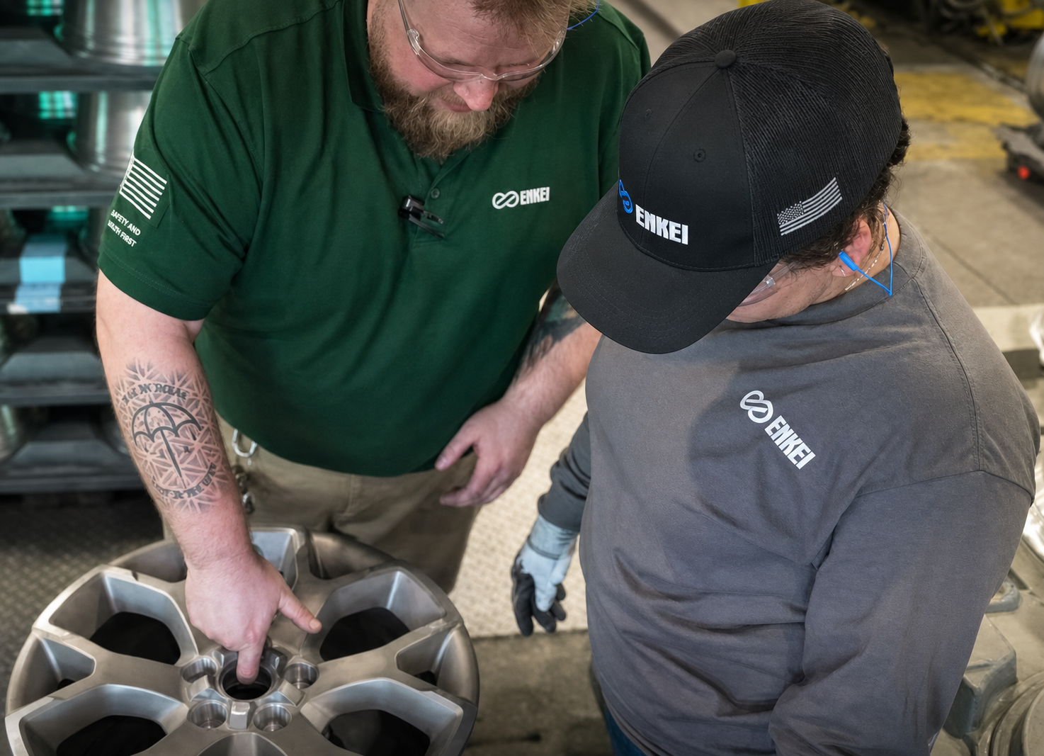 Two workers examining a metal wheel in a manufacturing setting, with one pointing at the wheel's features.